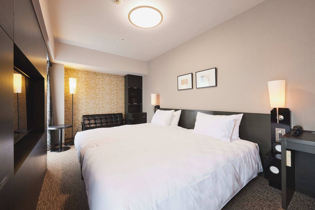 A hotel room with a large bed, bedside tables, a desk, a chair, a TV, and artwork on the wall.