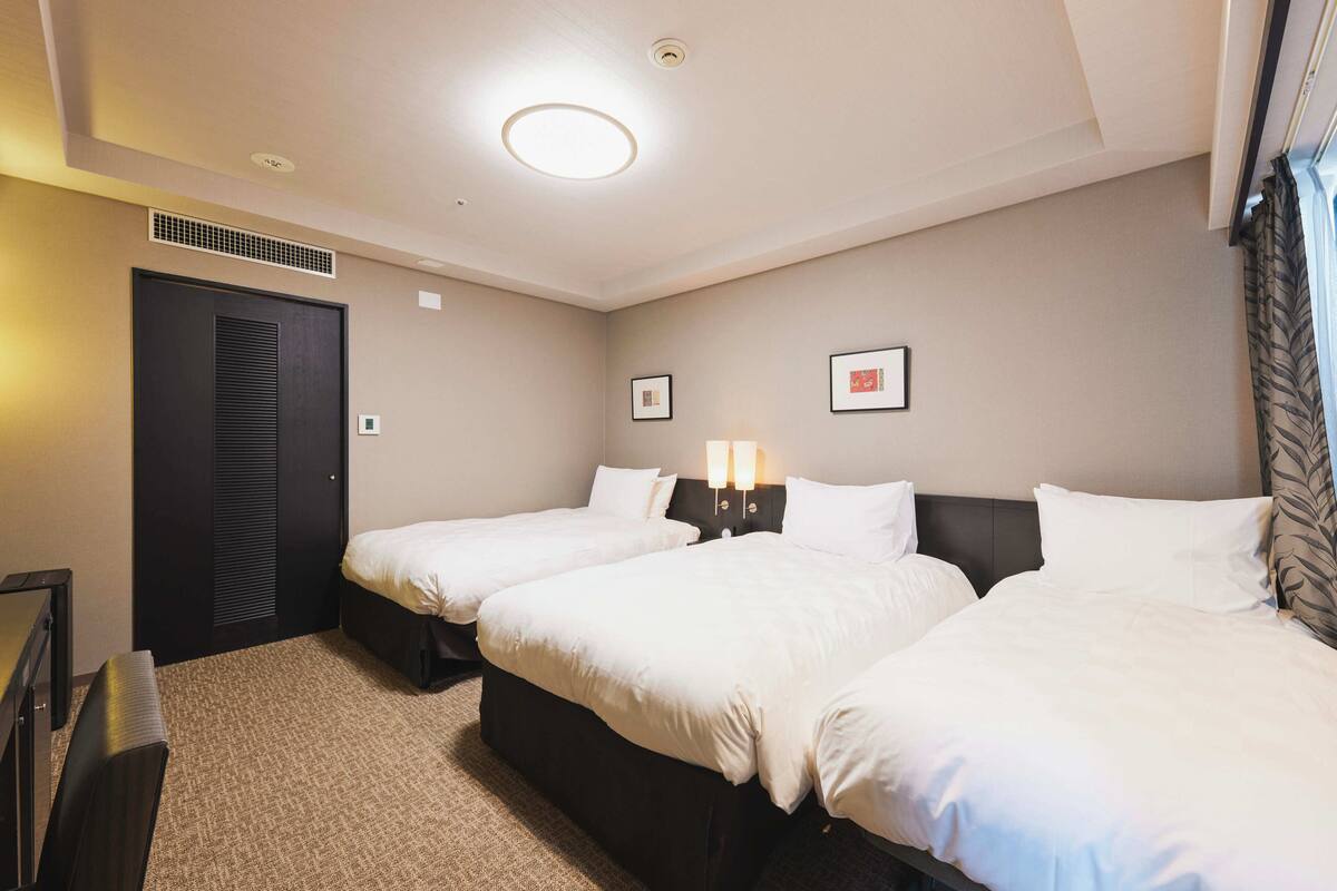 A hotel room with two beds, a desk, a chair, a wardrobe, and a ceiling light.