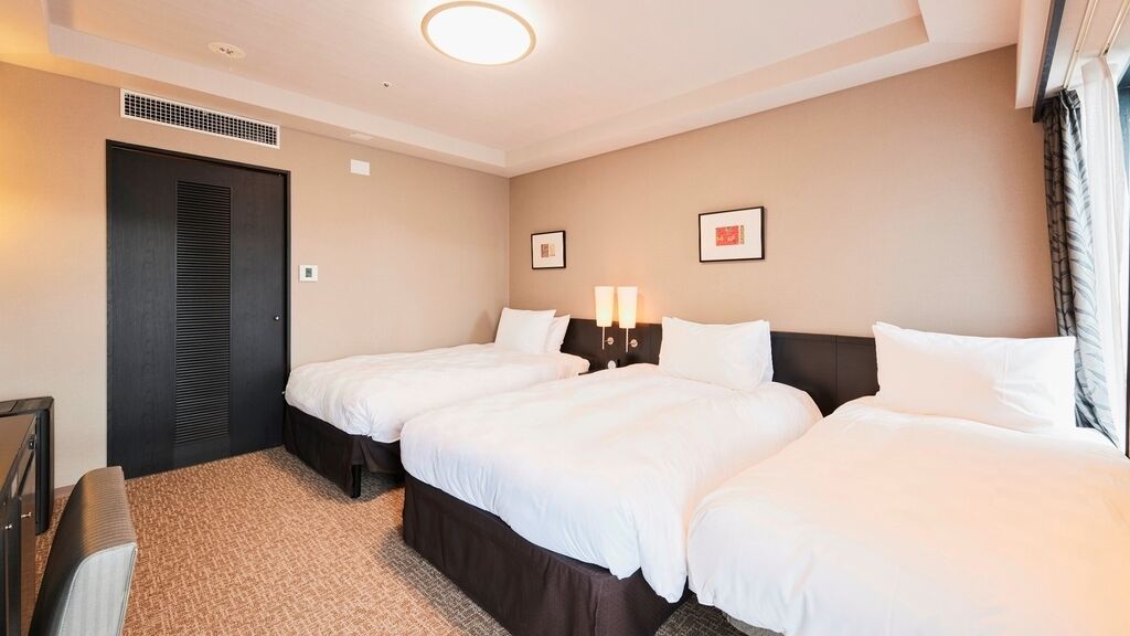 Ein Hotelzimmer mit zwei Betten, einem dunkelbraunen Kleiderschrank, einem kleinen Schreibtisch und einer Wandleuchte.