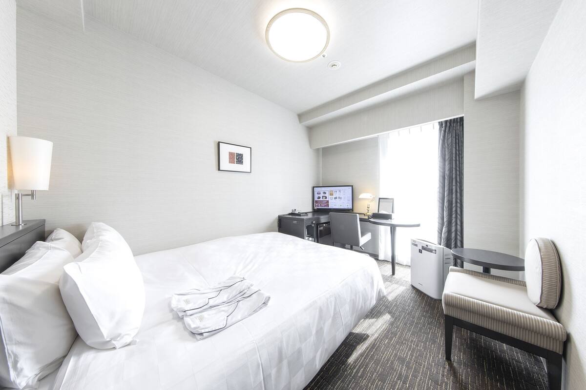 A hotel room with a bed, a desk, a chair, and a TV.