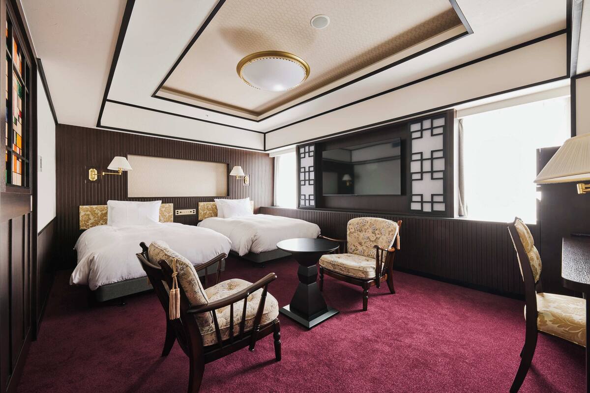 A hotel room with a large bed, two bedside tables, a small round table, and three chairs.