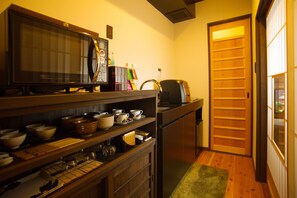 A compact kitchen with a microwave, shelves with bowls and cups, a refrigerator, and a wooden door.
