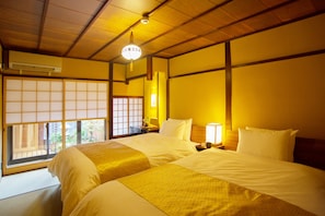 A traditional Japanese-style room with tatami flooring, two beds with white bedding, a shoji screen window, and a ceiling fan. - Kyo Ryokan Gekko-an (Kyoto)