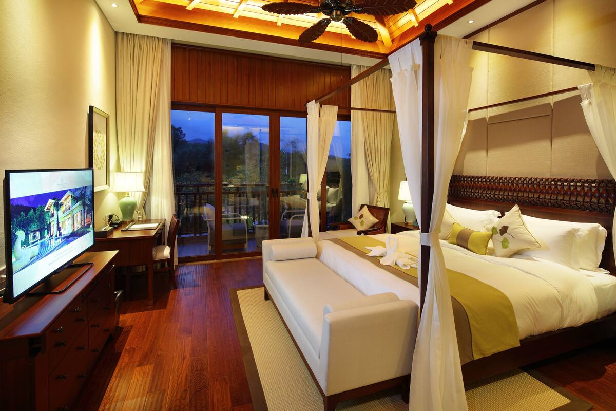 Een moderne slaapkamer met een groot bed, een televisie, een bank en een balkon met gordijnen.