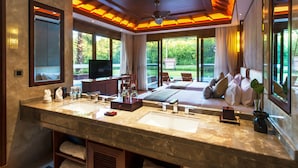 A luxurious bathroom with a large marble sink, a ceiling fan, and a view of a garden through large windows.