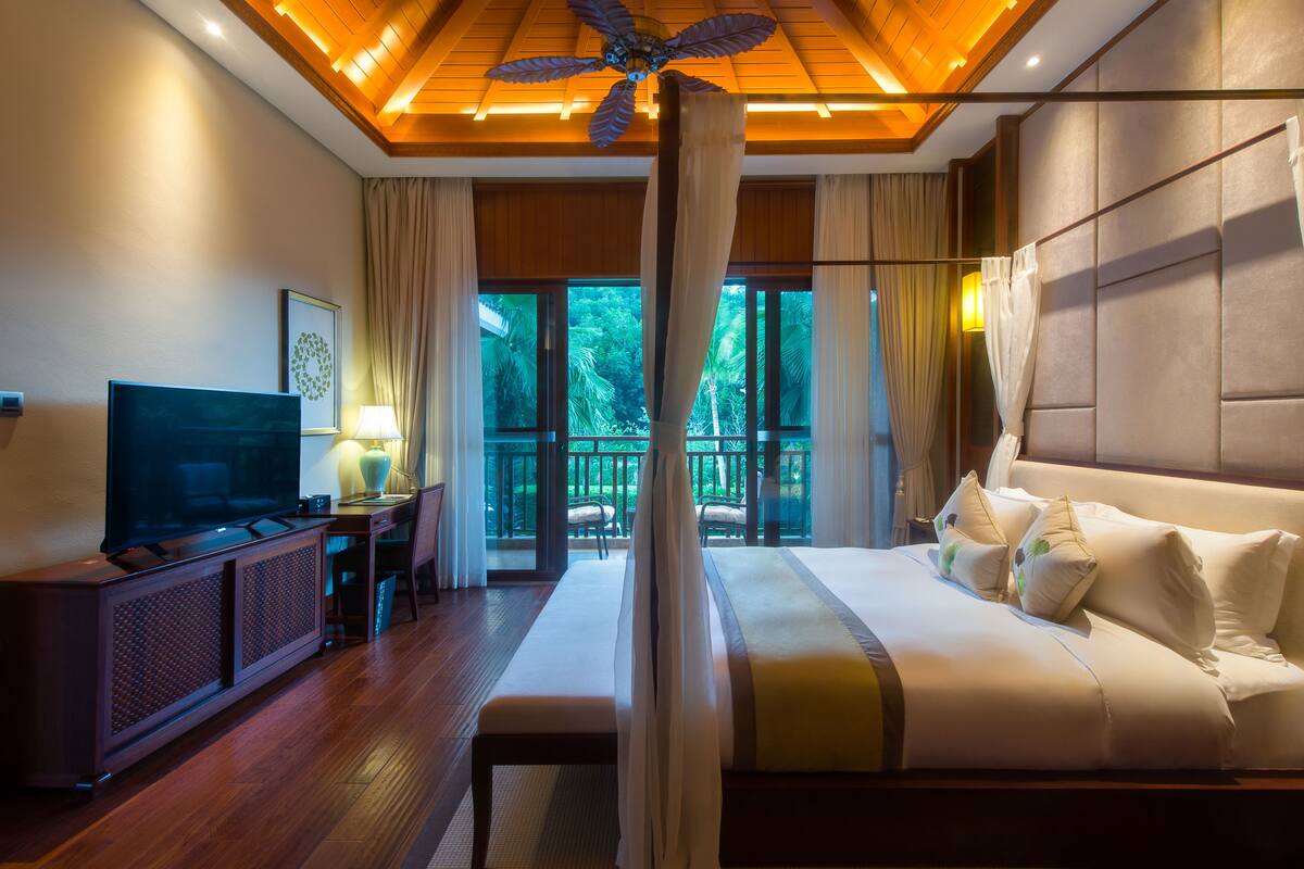 Een hotelkamer met een groot bed, een televisie, een bureau met een lamp en uitzicht op het landschap door grote ramen.