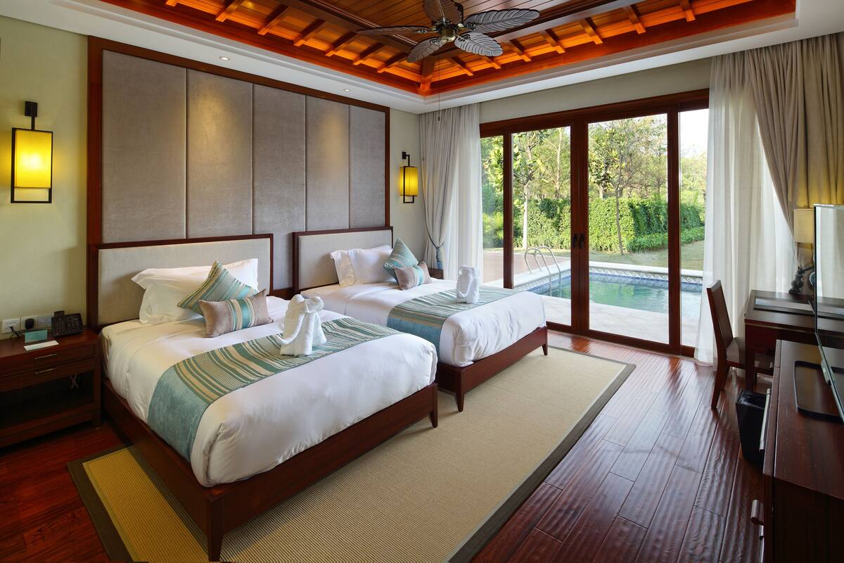 Een hotelkamer met twee bedden, een houten plafond en uitzicht op de omgeving.