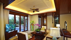 A spacious living room with a television, comfortable seating, a coffee table, and a large window offering a view of the outdoors.