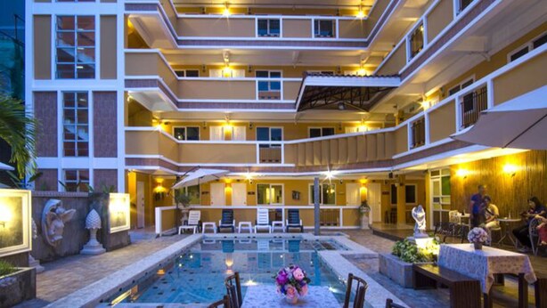 A multi-story hotel with a central pool area, outdoor seating, and a well-lit facade.