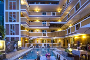 A multi-story hotel with a central pool area, outdoor seating, and a well-lit facade.