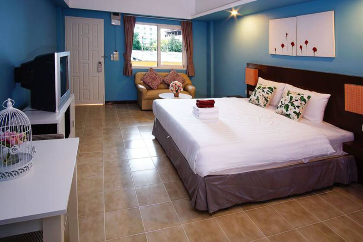 Une chambre d’hôtel avec un lit, une télévision, un canapé et une fenêtre avec des rideaux.