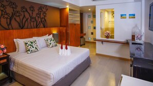 A hotel room with a large bed, a wooden headboard, a bedside table with a lamp, a desk with a chair, and a decorative wall panel.