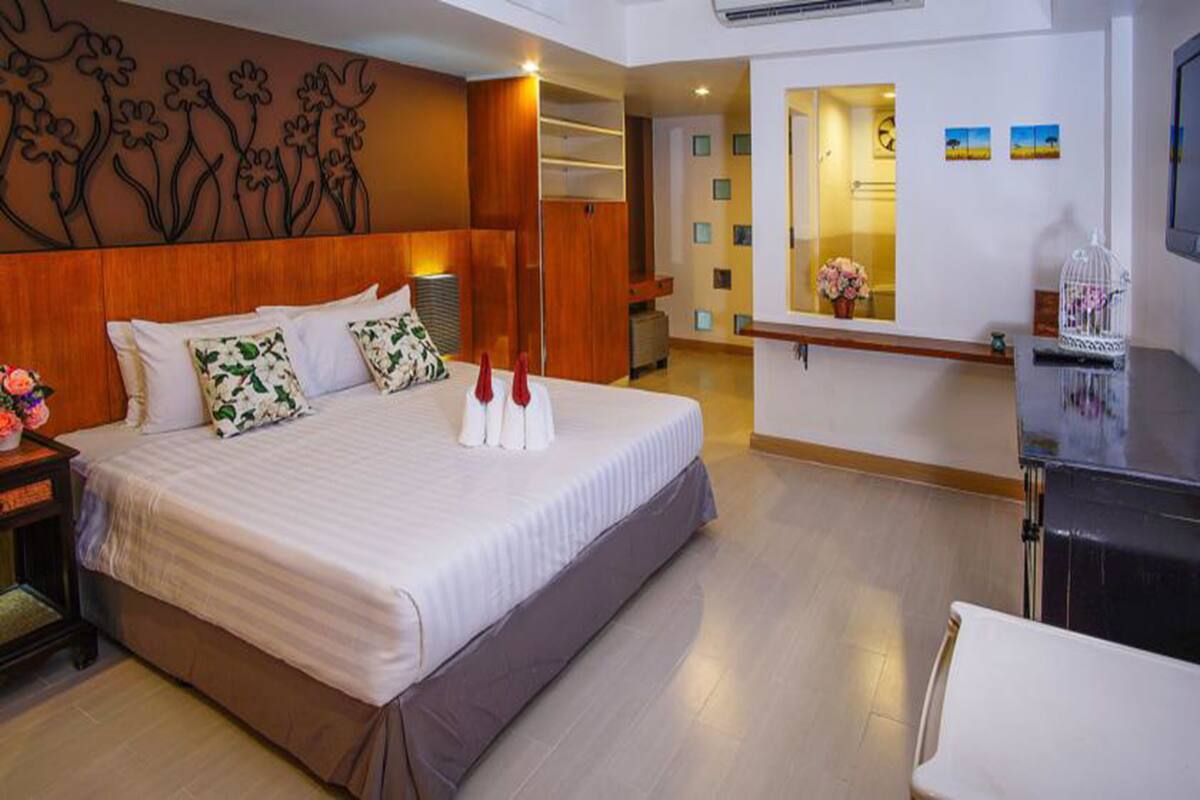 Une chambre d’hôtel avec un grand lit, une tête de lit en bois, une table de chevet avec une lampe, un bureau avec une chaise et un panneau décoratif au mur.