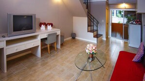 A modern living room with a TV, a desk, a chair, a glass coffee table with flowers, and a staircase leading to another room.
