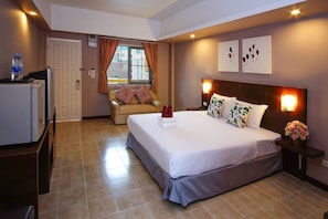 A hotel room with a bed, a chair, a desk, a refrigerator, and a window with curtains.