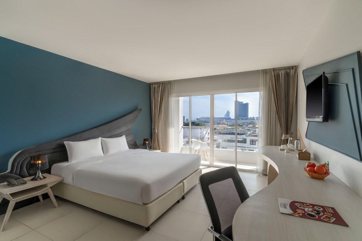 Une chambre d’hôtel équipée d’un lit, d’un bureau, d’une chaise et d’une grande fenêtre donnant sur la ville.