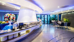 A modern hotel lobby with a buffet area, seating arrangements, and a large decorative vase. - Blue Boat Hotel JC (Pattaya)
