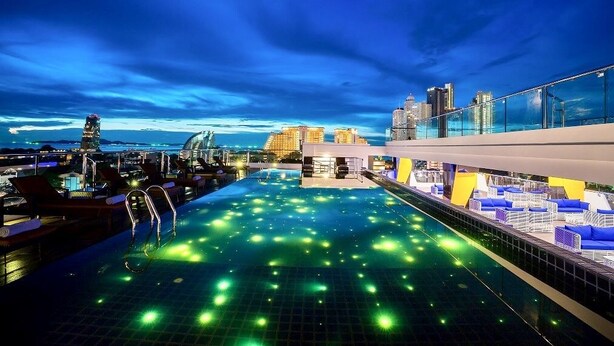 A rooftop infinity pool with city views, lounge chairs, and a glass railing. - Blue Boat Hotel JC (Pattaya)