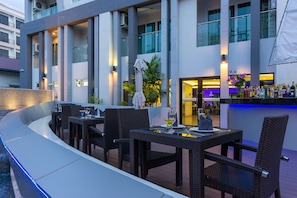 An outdoor dining area with tables and chairs, a pool, and a bar with a neon sign. - Blue Boat Hotel Pattaya (Pattaya)