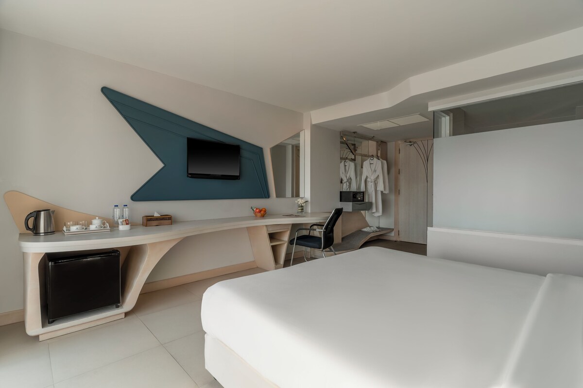 A modern hotel room with a bed, desk, and TV.