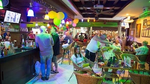 Uma área de bar com cadeiras de vime, um balcão com garrafas e um ventilador de teto.