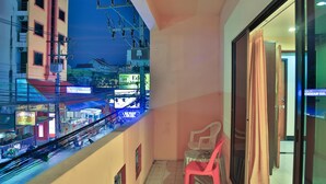 Uma varanda com vista para uma rua movimentada, uma mesa com cadeiras e uma porta que dá para outro cômodo.