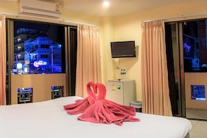 A hotel room with a bed, a flat-screen TV mounted on the wall, and a view of the cityscape through the window. - Harrys Hotel, Bar & Restaurant (Pattaya)