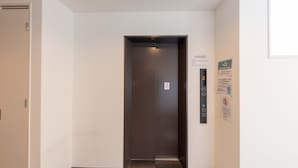 A narrow hallway with a closed elevator door, a door on the left, and a wall with a sign indicating a smoking area. - MUSUBI KYOTO Higashiyama Gojo (Kyoto)