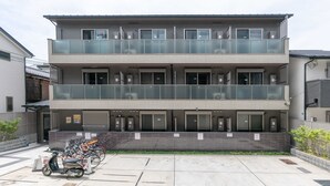 A modern two-story building with a glass balcony on the upper floor, a parking area with scooters, and a gated entrance. - MUSUBI KYOTO Higashiyama Gojo (Kyoto)