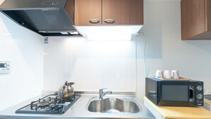 A compact kitchen with a gas stove, stainless steel sink, and a microwave. - MUSUBI KYOTO Higashiyama Gojo (Kyoto)