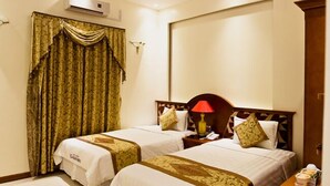 Una habitación de hotel con dos camas, una mesita de noche con lámpara y un ventanal con cortinas.