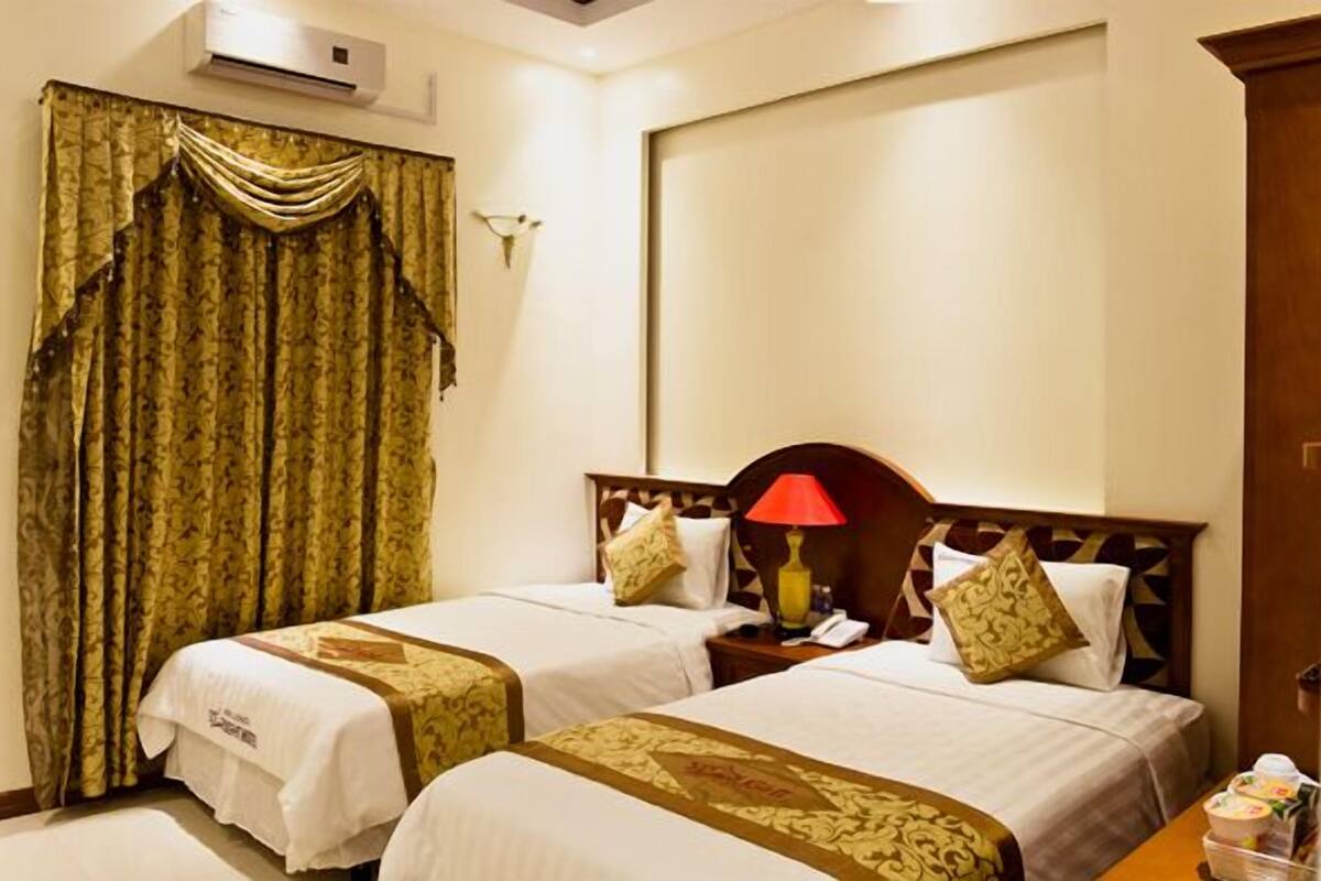 Una habitación de hotel con dos camas, una mesita de noche con lámpara y un ventanal con cortinas.