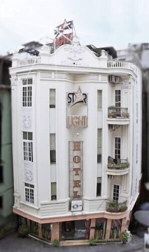 Un immeuble blanc à plusieurs étages, dont la façade porte une enseigne indiquant « HÔTEL » et « LUMIÈRE ».