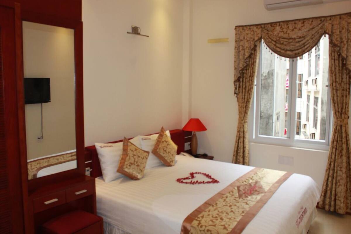 Una habitación de hotel con cama, una lámpara roja, un espejo y una ventana con cortinas.