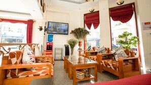 Un vestíbulo de hotel con muebles de madera, un televisor y ventanas amplias con cortinas rojas.