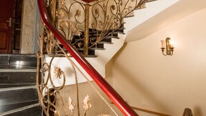 Una imponente escalera con barandales de metal decorados y un pasamanos rojo.