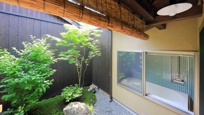 Una stanza con soffitto in legno, una finestra con telaio a griglia e un piccolo giardino con piante e rocce.