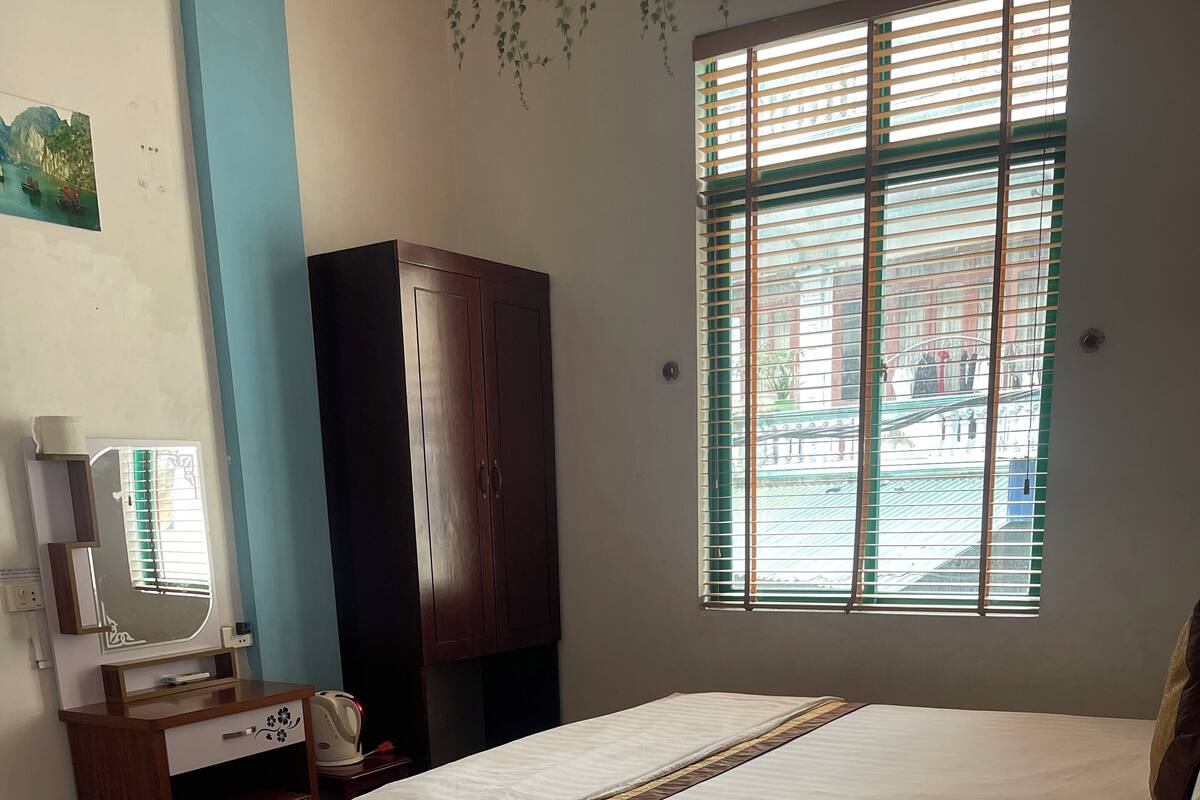 Une chambre d’hôtel avec deux lits, une armoire en bois, un bureau avec un miroir et une fenêtre avec des stores.