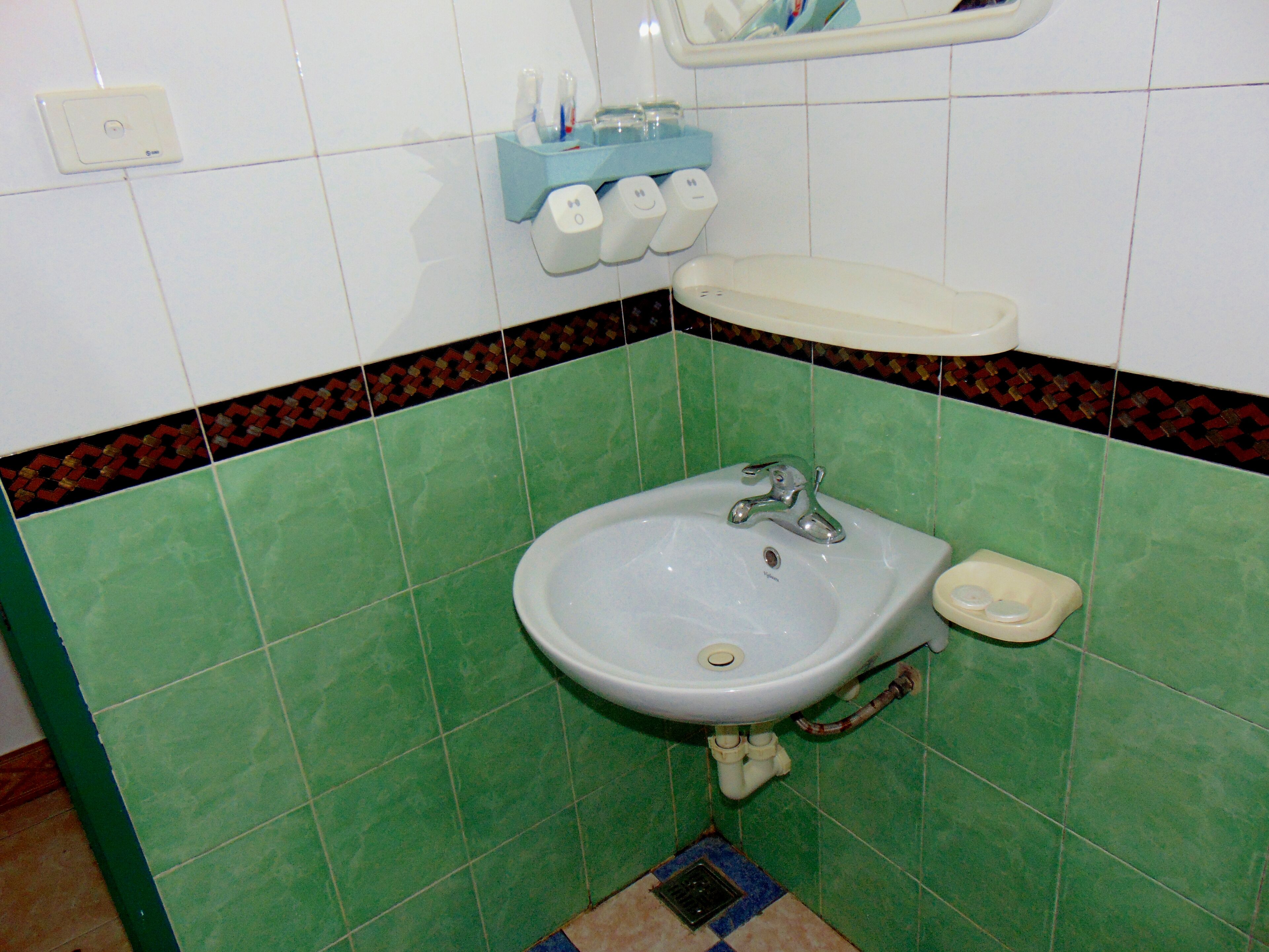 Une salle de bain avec un lavabo, un miroir et des murs recouverts de carreaux verts.
