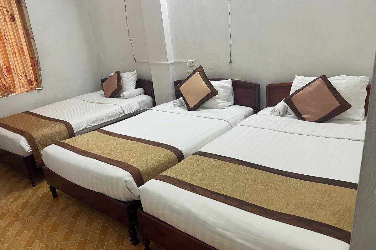 Une chambre d’hôtel avec trois lits simples, chacun doté d’une tête de lit marron et de draps blancs.