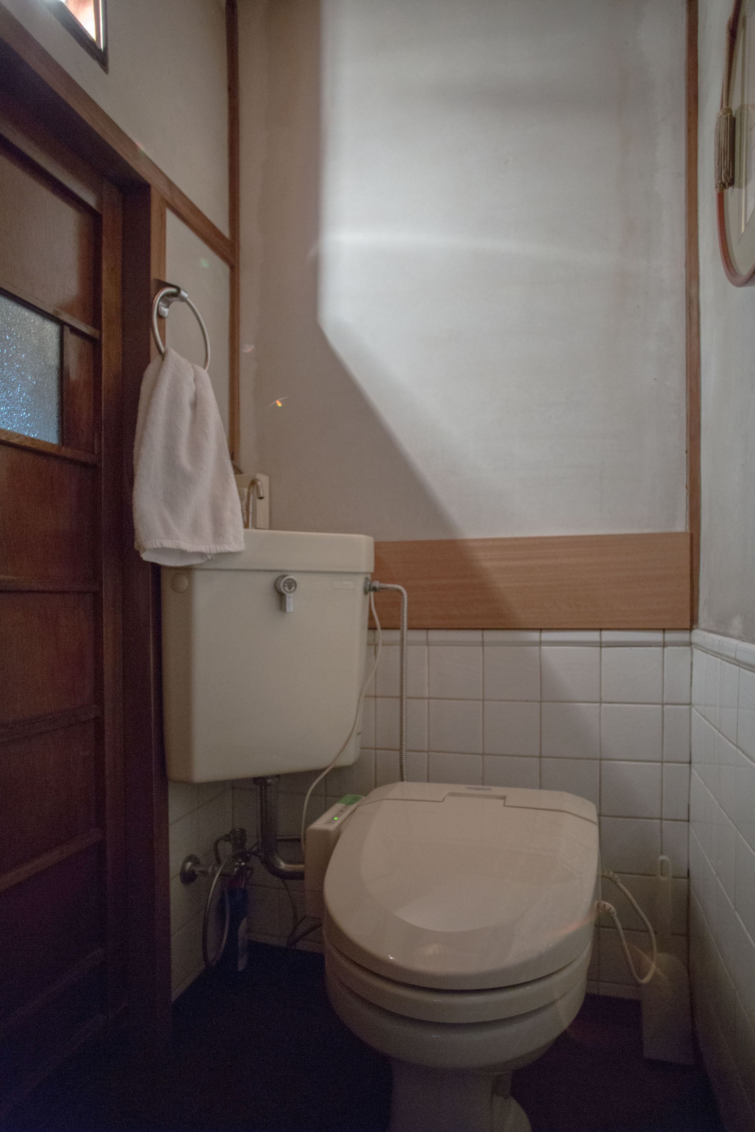 A bathroom with a toilet, a towel hanging on the wall, and a window with blinds.