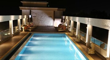 Una piscina rectangular con cubierta de madera, rodeada de barandillas de vidrio y sillas de descanso.