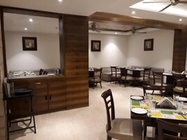 A dining area with multiple tables and chairs, a wooden cabinet, and ceiling fans.