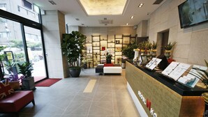 Zona de recepción de hotel con mostrador, asientos y plantas en macetas.