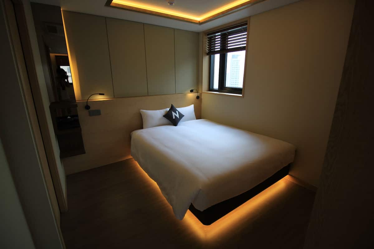 Une chambre moderne avec un grand lit, une armoire intégrée et une fenêtre équipée de stores.