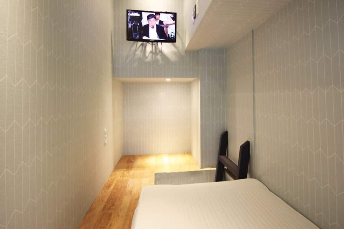 Une chambre d’hôtel avec un lit, un téléviseur fixé au mur et un plancher en bois.