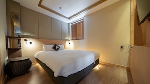 Un dormitorio moderno con una cama grande, una mesita de noche pequeña, una lámpara de pared y una ventana con persianas.