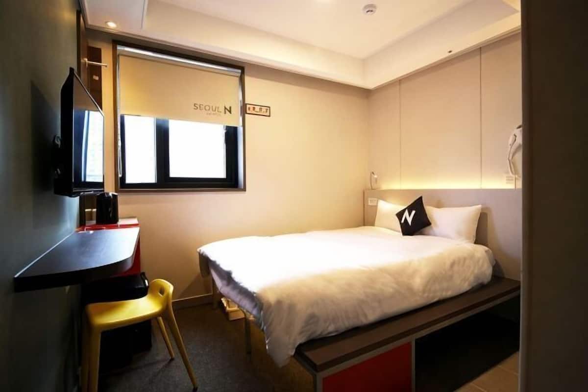 Une chambre d’h ôtel avec un lit, un bureau, une chaise, une télévision et une fenêtre avec une pancarte.