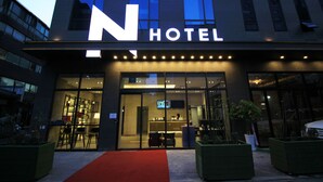 Un hotel moderno con un llamativo letrero 'N HOTEL', amplios ventanales de vidrio y una alfombra roja que conduce a la entrada.