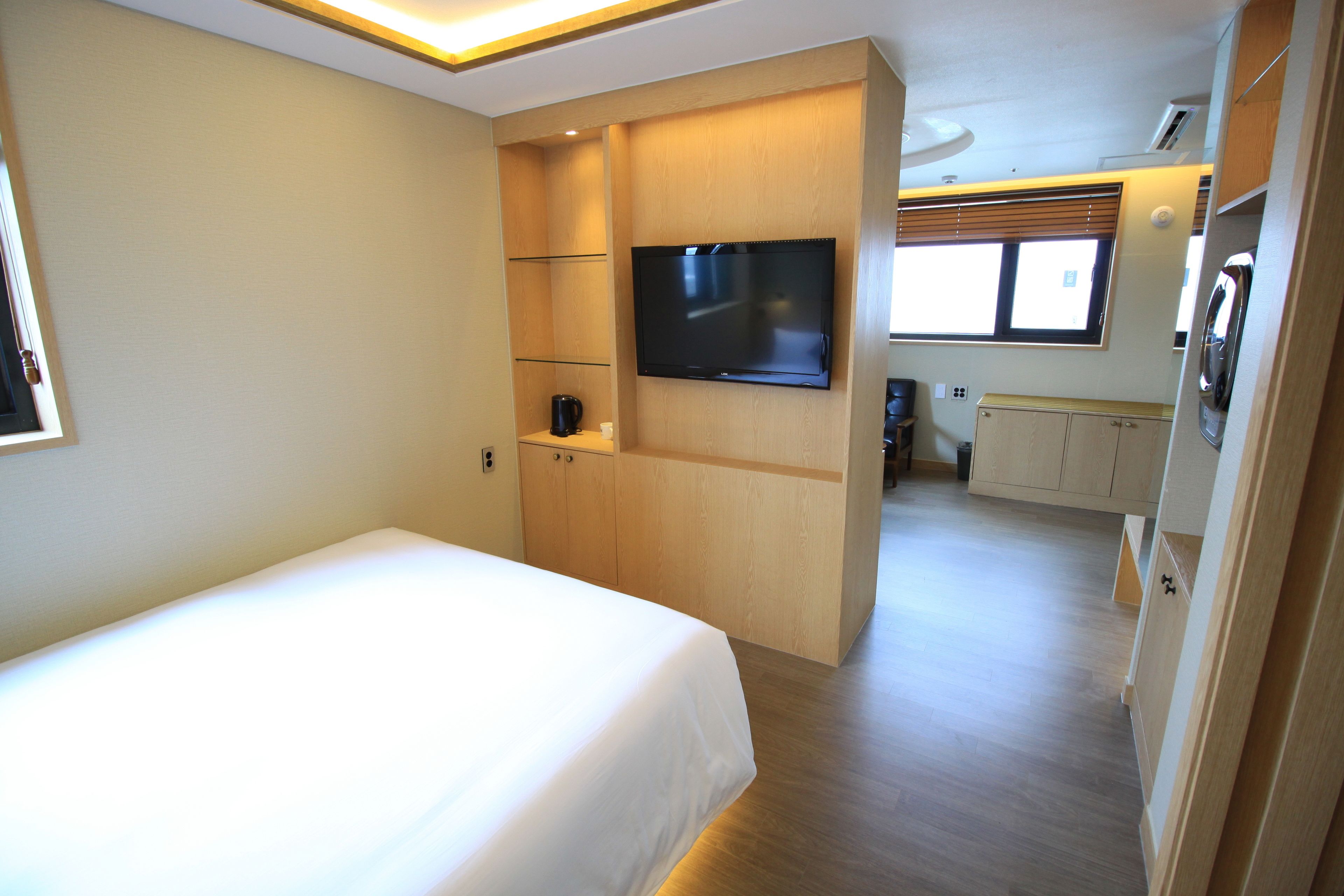 A bedroom with a bed, a television mounted on the wall, and a kitchenette area with cabinets and a microwave.